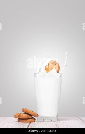 Chocolate Chip Cookie spritzt in ein volles Glas Milch mit Cookies auf der Seite auf einem texturierten Wandhintergrund mit Platz und Platz für Text kopieren Stockfoto