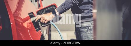 Der Mann lädt das Elektroauto an der Ladestation auf. Stockfoto