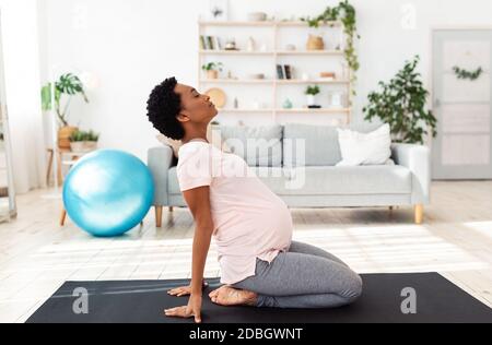Seitenansicht der schwarzen schwangeren Frau, die während der Meditation Backbend macht Oder Yoga zu Hause Stockfoto