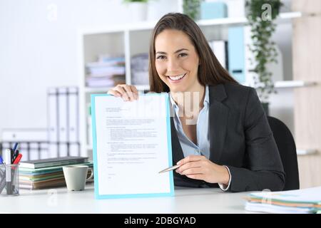 Vorderansicht einer fitschigen Exekutive Frau zeigt Vertrag Unterschrift Raum mit Stift Blick auf Kamera sitzt auf einem Schreibtisch im Büro Stockfoto