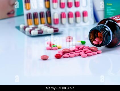 Tabletten Pillen aus bernsteinfarbener Glas Medikamentenflasche auf verschwommenen Kapseln in Blisterverpackung verteilt. Rote und rosa Tabletten. Konzept für die Verwendung von Medikamenten. Schmerzmittel medi Stockfoto