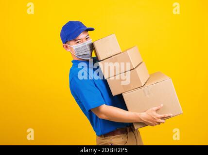 Asiatische junge Lieferarbeiter Mann in blauen T-Shirt und Mütze Uniform tragen Gesichtsmaske Schutz Heben Stapel eine Menge Boxen, unter Coronavirus oder COVID- Stockfoto