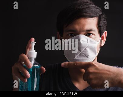 Nahaufnahme Asian schöner Mann trägt schützende Gesichtsmaske mit Angst in Auge halten und Punkt Desinfektionsmittel Gel, Hygiene Prävention COVID-19 Virus oder Coronav Stockfoto