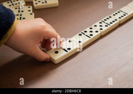 Kind spielt Dominosteine auf Holztisch. Detail der Hand des Kindes und Domino Fliesen von oben gesehen. Pädagogische Spiele, Entwicklung und Indoor-Aktivitäten Stockfoto