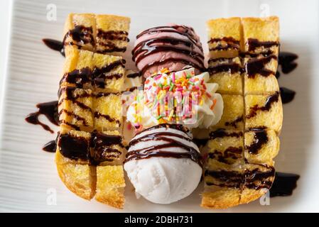 Nahaufnahme Draufsicht Honig Toast Brot serviert Vanille Kokosmilch Eis Schaufel mit Schokoladensirup dekorieren und Sahne Zucker Topping in einem Whi bestreuen Stockfoto