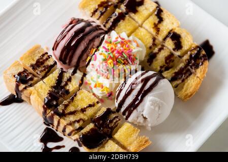 Nahaufnahme Draufsicht Honig Toast Brot serviert Vanille Kokosmilch Eis Schaufel mit Schokoladensirup dekorieren und Sahne Zucker Topping in einem Whi bestreuen Stockfoto