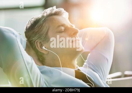 Reifer Geschäftsmann schläft während der Musikwiedergabe mit Ohrhörern am Flughafen mit Linsenflauschen Stockfoto