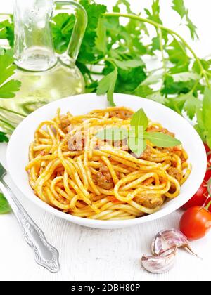 Spaghetti Pasta mit Sauce Bolognese von Hackfleisch, Tomatensaft, Knoblauch, Wein und Basilikum in einem Teller, Pflanzenöl, würzige Kraut auf einem leichten Holzschwein Stockfoto