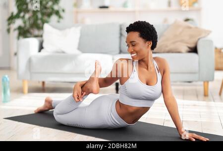 Inländisches Sportkonzept. Athletische junge schwarze Frau in Sportkleidung, die Fitness-Übungen auf Yoga-Matte innen macht Stockfoto