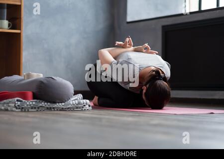 Junge Frau, die in Kinderpose auf einer Yogamatte sitzt Stockfoto