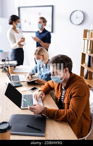 Junge multikulturelle Geschäftsleute in medizinischen Masken arbeiten im Freien Office während Quarantäne auf unscharfem Hintergrund Stockfoto