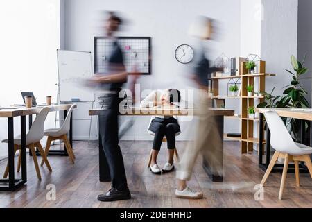 Erschöpfte afroamerikanische Geschäftsfrau schläft auf dem Schreibtisch im offenen Raum Büro, Bewegungsunschärfe Stockfoto