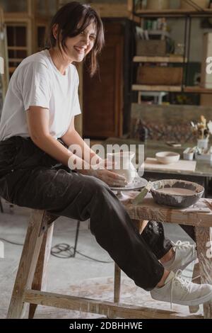 Schöne lachende Frau arbeitet auf Töpfer Rad Herstellung Tonkrug in Töpferei. Stockfoto