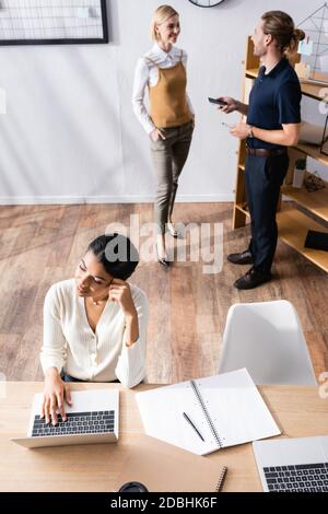 Blick von oben auf eine afroamerikanische Frau, die am Schreibtisch saß Notebook mit Büromitarbeitern im Hintergrund Stockfoto