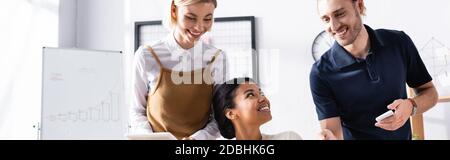 Glückliche Büroangestellte in der Nähe afroamerikanische Frau während der Diskussion am Arbeitsplatz, Banner Stockfoto