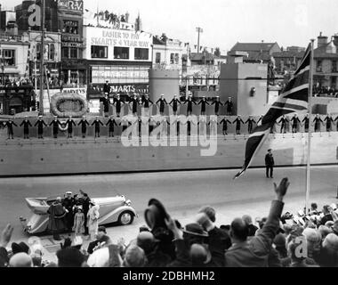 "Vor dem Auto, von rechts nach links: König George VI., Prinzessin Elizabeth und Königin Elizabeth bei der Royal Navy Review in Portsmouth. Junge Jungen in Seemannsuniform stehen auf einem dekorierten Kriegsschiff. Die Häuser sind mit Girlanden und Schildern mit der Aufschrift "lang lebe die Erbin Majestät" dekoriert." Stockfoto