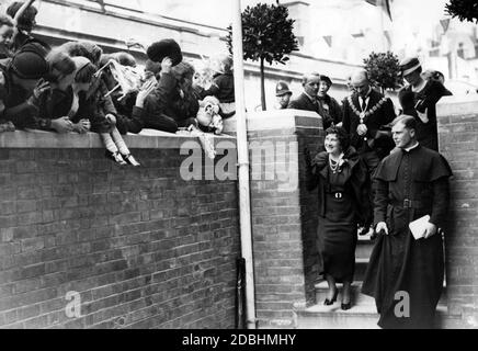 Elizabeth, Herzogin von York, bei der Einweihung der Basil Jellicoe Hall und eines neuen Wohnblocks in Drummnond Crescent, Somers Town in London. Das Sozial- und Arbeitszentrum wurde als Denkmal für den jungen, verstorbenen Priester Basil Jellicoe gegründet, der 1935 ein Londoner Slum in eine Gartenstadt verwandelte. Die Herzogin wird von den Bewohnern und ihren Kindern mit Lächeln und Wellen begrüßt. Stockfoto