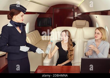 Das Kabinenpersonal bedient Passagiere der Business-Klasse im Flugzeug. Air Hostess bedient weibliche Passagiere im Privatjet. Stockfoto