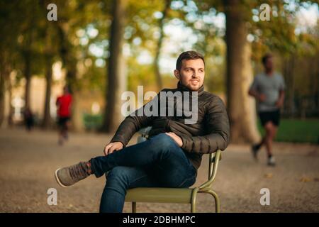 Ein hübscher Mann sitzt mitten im Park Khaki Hocker Stockfoto