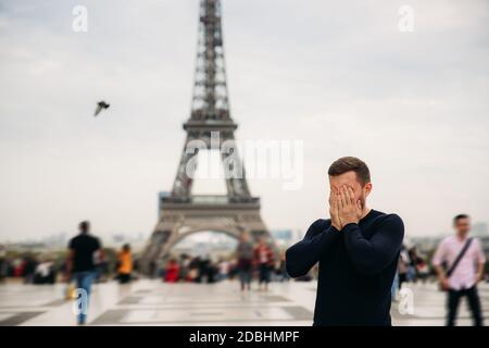 Fröhlicher Mann im dunkelblauen Pullover steht auf dem Hintergrund des Eiffelturms Stockfoto