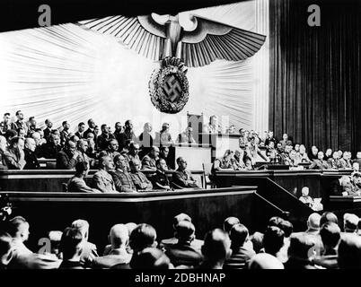 Adolf Hitler während seiner Rede über die Kriegserklärung an die USA. Links von Hitler sind Julius Schaub und Hans Heinrich Lammert, rechts Otto Dietrich und Albert Bormann. Über ihm, Reichstagspräsident Hermann Göring. Neben Hitlers freiem Sitz auf der Regierungsbank sind Joachim von Ribbentrop, Erich Raeder, Walther von Brauchitsch, Wilhelm Keitel, Wilhelm Frick und Joseph Goebbels. Auf der Bank oben, von rechts sitzend: Johann Ludwig Graf Scherin von Krosigk, Walther Funk, Walter Darre, Bernhard Rust, Hanns Kerrl, Hans Frank, Julius Dorpmueller, Arthur Seys Inquart und Fritz Todt. Stockfoto