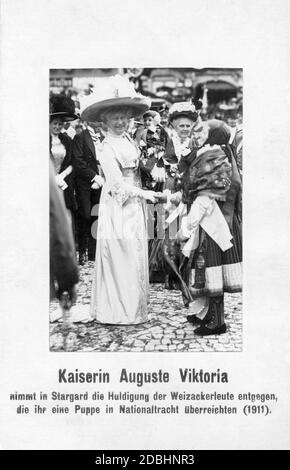 Kaiserin Auguste Viktoria wird 1911 in Stargard in Pommern (heute Szczecinski in Polen) von Weizacker begrüßt. Sie überreichten ihr eine Puppe in ihrer Nationaltracht, die die Kaiserin in der Hand hält. Stockfoto