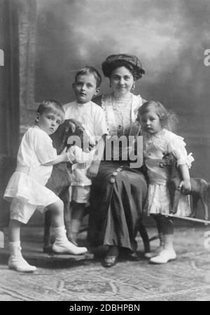 Hermine Reuss Elder Line mit ihren drei ältesten Kindern, von links nach rechts: Prinz Georg Wilhelm von Schoenaich-Carolath, Prinz Hans Georg von Schoenaich-Carolath, Hermine Reuss Elder Line und Prinzessin Hermine Karoline von Schoenaich-Carolath. Die Kinder haben ein Schaukelpferd und ein weiteres Spielzeugpferd zum Spielen. Das Bild wurde um 1913 aufgenommen. Stockfoto