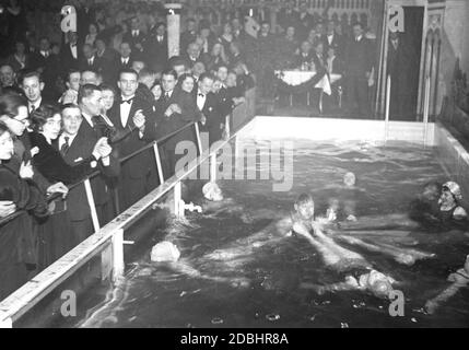 "Im neuen Tanzpalast in Berlin-Mitte, dem ehemaligen Alten Ballhaus in der Joachimstraße, wurde als Attraktion ein Schwimmbad gebaut, in dem Frauen und ein Mann baden. Auf der linken Seite beobachten die Gäste von der Tanzfläche aus. Der Trend des Badens in Tanzpalästen wurde von Paris übernommen. Das Bild wurde 1931 aufgenommen." Stockfoto