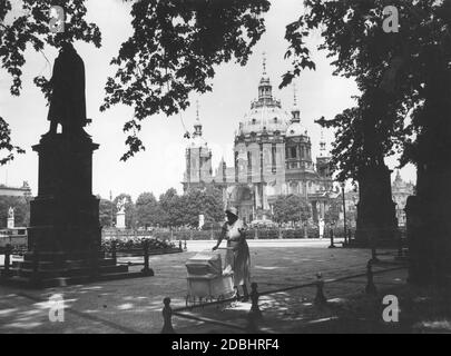 Eine Mutter nimmt ihr Kind an einem heißen Sommertag 1930 mit auf einen Spaziergang unter den schattigen Bäumen des Schinkelplatzes. Im Hintergrund ist der Berliner Dom zu sehen. Die Statuen ehren Albrecht Daniel Thaer (links), Christian Peter Wilhelm Beuth (rechts) und Karl Friedrich Schinkel (ganz rechts). Stockfoto