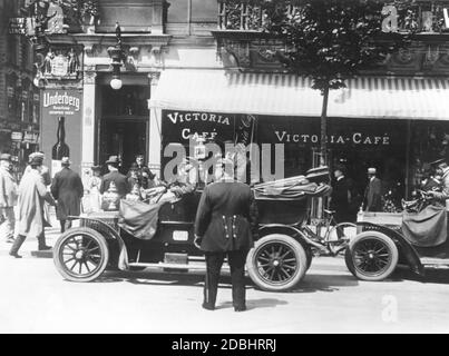 "Ein Auto hält vor dem Victoria-Cafe am Boulevard unter den Linden, Ecke Friedrichstraße in Berlin und ein Passagier steigt aus. An der Ecke hängt ein Werbeplakat für ''Underberg-Boonekamp SEMPER IDEM'' und darüber ein Schild für ''Patentbuero Lenck''. Das Bild wurde um 1920 aufgenommen." Stockfoto