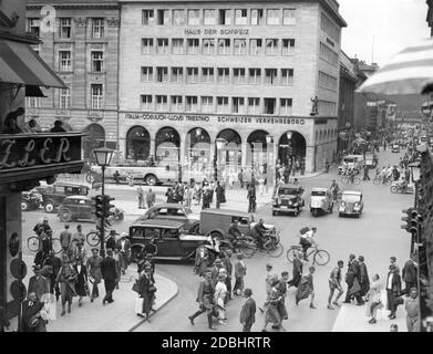 Blick von der Friedrichstraße in Berlin vom Cafe unter den Linden auf die Kranzler-Ecke (links), die Straße unter den Linden und das Haus der Schweiz mit den Tellknaben an der Ecke. An der verkehrsreichen Kreuzung im Herzen Berlins teilen sich Autos, Busse (Berolina Rundfahrten), Radfahrer, Motorräder und Fußgänger die Straße. Das Bild wurde 1937 aufgenommen. Stockfoto