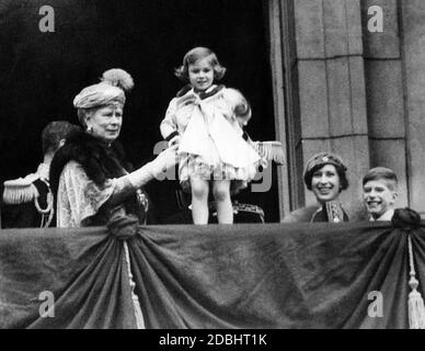 After the wedding of the Duke and Dutchess of Kent, King George V. holds up the baby Princess Margaret Rose on the balcony of Buckingham Palace. To her left stands Queen Mary. Stock Photo