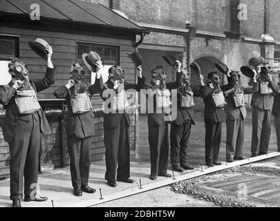 Während einer Demonstration der lokalen Luftverteidigungseinheiten in Westminster heben Mitglieder der zivilen Luftverteidigung ihre Hüte, während sie Atemschutzmasken tragen. Stockfoto