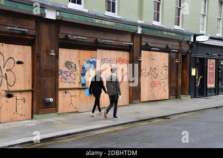 Ein paar Spaziergang vorbei an geschlossenen Cafés und Restaurants auf der Old Compton Street in Soho, London, während der zweiten nationalen Sperre in England. Stockfoto