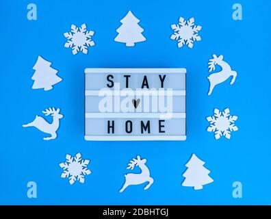 Leuchtkasten mit Stay Home Zitat auf blauem Hintergrund mit weihnachtsspielzeug. Stockfoto