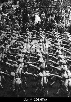 SA-Einheiten marschieren während des NSDAP-Kongresses durch Nürnberg. Sie werden von der Bevölkerung und von SS-Führern beobachtet, die in der Mitte lächeln. Links im Hintergrund sind mehrere Mercedes-Autos zu sehen. Stockfoto