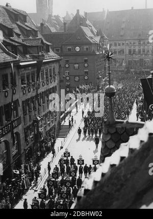 "AUF dem Weg zum sogenannten Adolf-Hitler-Platz MARSCHIEREN EINHEITEN über die Fleischbrücke. Auf dem Gebäude auf der anderen Seite der Brücke auf der linken Seite gibt es mehrere Hakenkreuze und ein Schild mit der Aufschrift ''Heil dem Führer!'' (''Gegrüßet dem Führer''). Unten links, inmitten der Zuschauer, sind mehrere Krankenschwestern." Stockfoto