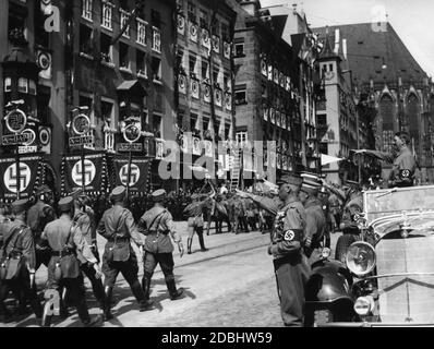 Adolf Hitler, der in seinem Mercedes steht, grüßt die Standardträger der SA auf dem Nürnberger Hauptmarkt, dem sogenannten Adolf-Hitler-Platz. Vor ihm links Franz Pfeffer von Salomon, rechts Viktor Lutze. Im Hintergrund ist ein Teil der Sebaldus-Kirche. Stockfoto