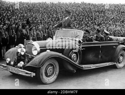 Adolf Hitler wird in einem Mercedes von Mitgliedern der Hitlerjugend und des BDM im Hitler-Jugendstadion begrüßt. Rudolf Hess und Baldur von Schirach sitzen auf dem Rücksitz. Links neben Hess befindet sich der Fotograf Heinrich Hoffmann. Stockfoto