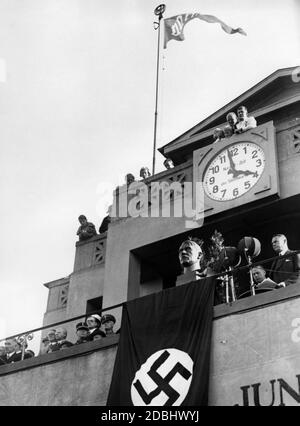 'Beim 'Festival der Deutschen Schule' im Berliner Grunewald-Stadion ist eine Büste des abwesenden Adolf Hitler auf dem VIP-Stand über einer Hakenkreuzflagge zu sehen. Über ihm ist eine Uhr, die nach der Standardzeit des Observatoriums eingestellt ist. An einem Fahnenmast hängt eine Fahne des Veranstalters ''Volksbund für das Deutschtum im Ausland'', VDA.' Stockfoto