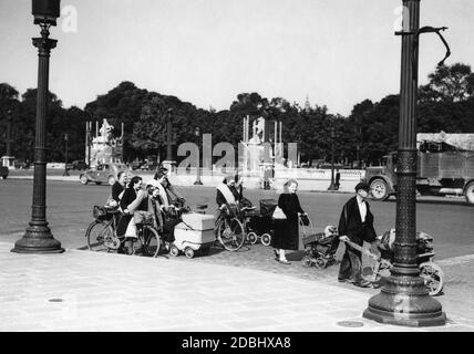 Frauen mit Kinderwagen und Gepäck gehen über den Place de la Concorde in Paris. Stockfoto