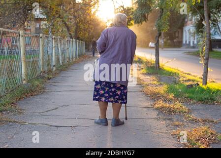 Alte Frau Großmutter mit einem Stock, lahm, etwa achtzig, auf der Straße alte Frau zu Fuß entlang der Stadtpromenade Stockfoto