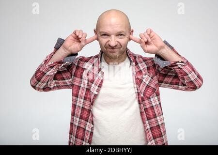 Kaukasische kahle, unrasierte Mann bedeckte Ohren mit Zeigefinger, um nicht zu hören. Stockfoto