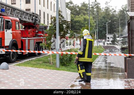 Feuerwehrmänner tragen Uniform hinter Feuerband und viele Feuer stehen Motorfahrzeuge mit Leiter bei Unfall im Hochhaus Wohngebäude Oder Bürogebäude Stockfoto