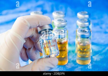 Corona-Virus und Covid - 19 Ärzte Hand hält einen Impfstoff, neuen Impfstoff in Flaschen, verschiedene Farbvariationen der Impfstoff-Flüssigkeit auf dem blauen Hintergroun Stockfoto