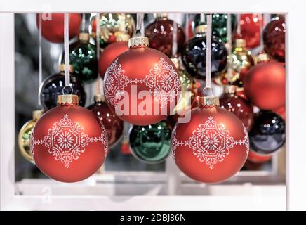 Rote Weihnachtskugeln mit Winterornamenten in einem weißen Rahmen. Neujahrsspielzeug auf Fäden. Stockfoto