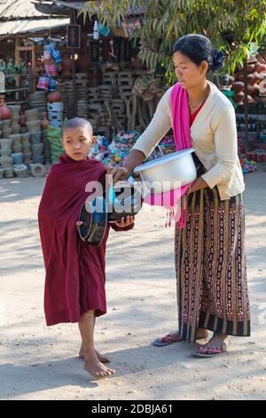 Novize buddhistischen Mönch sammeln Almosen in Bagan, Myanmar (Burma), Asien im Februar - lokale Frau geben Reis und Essen Stockfoto