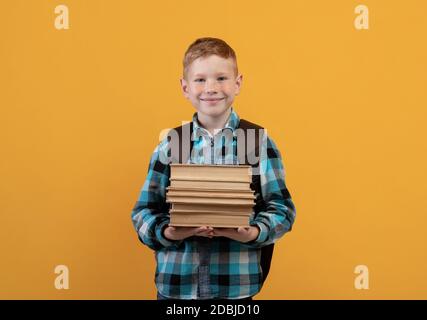 Lächelnder Schuljunge mit Rucksack, der viele Bücher hält Stockfoto