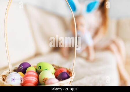 Niedliches lustiges Baby mit Kaninchenohren kriecht in den Korb Mit Ostereiern zu Hause auf dem Sofa Stockfoto