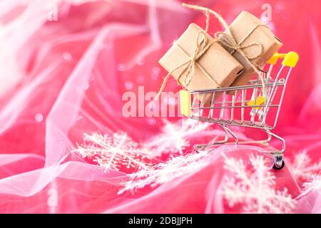 Kleiner Wagen mit Weihnachtsgeschenken. Weihnachtsgeschenke in Bastelpapier in einem Einkaufswagen auf rotem Hintergrund verpackt. Weihnachts- und Weihnachtsgeschenk-Konzept. Speicherplatz kopieren. Blick von oben. Draufsicht Stockfoto